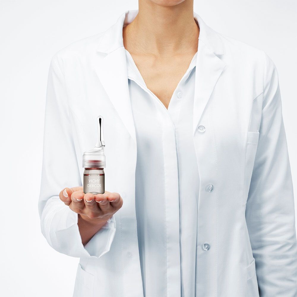 Een ampul in de hand van een persoon in een witte labojas. Opschrift: Vichy Dercos.