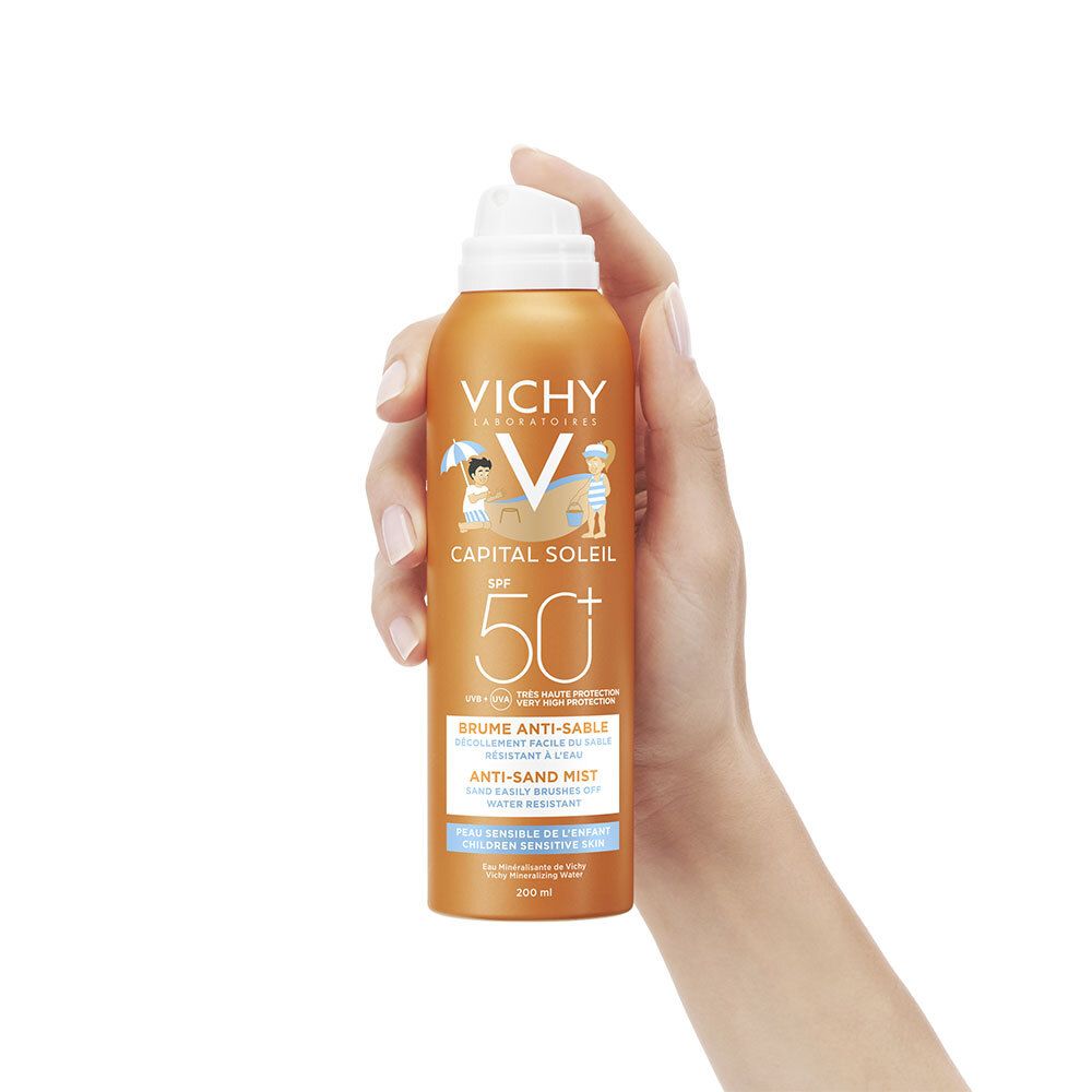 Hand hält Sonnencreme-Spray. Orangefarbene Dose mit weißem Sprühkopf. Vichy-Logo und SPF 50+.