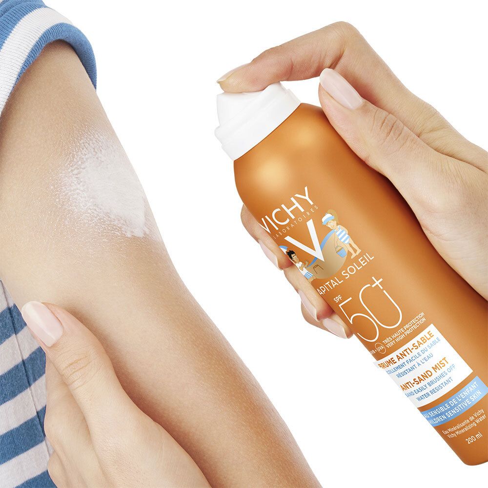 Hand sprüht Sonnencreme auf Arm. Orangefarbene Dose mit weißem Sprühkopf. Sichtbare weiße Flüssigkeit.