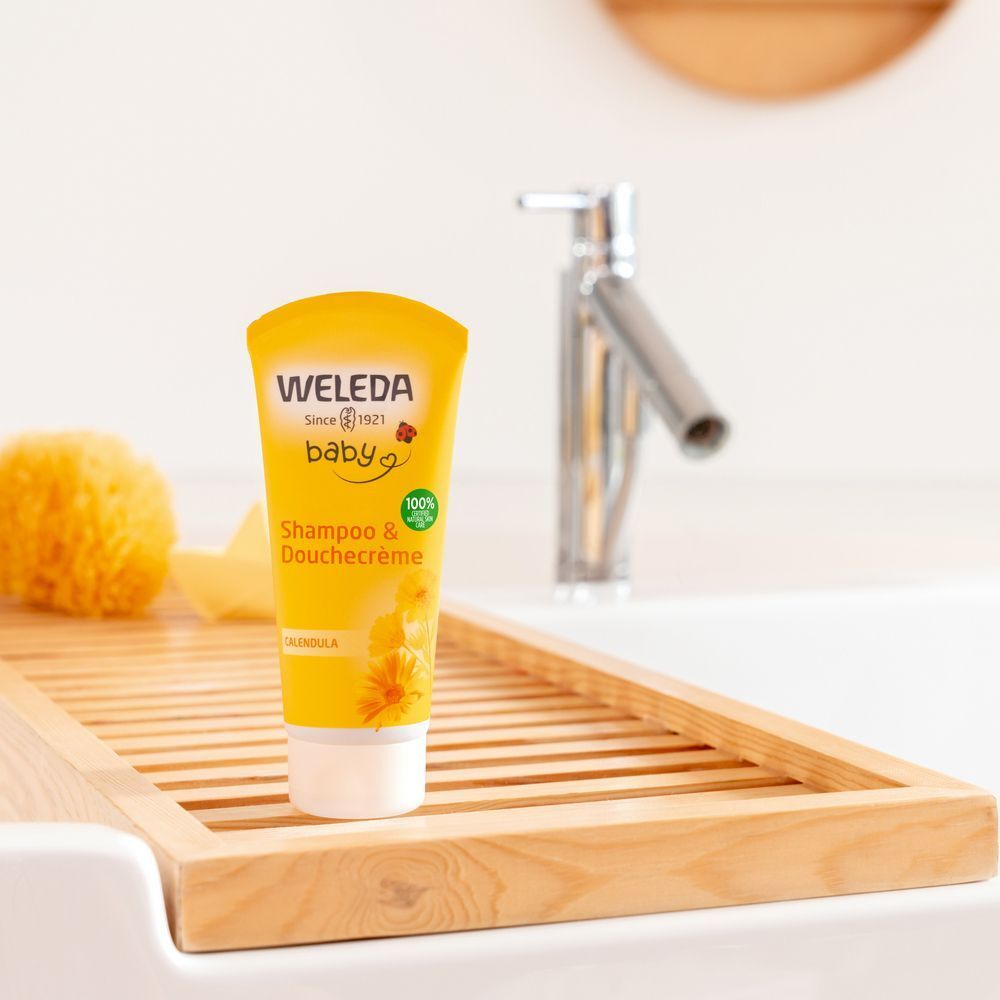 Gele tube "Weleda Baby" op houten plank in wastafel. Kraan op de achtergrond. Productnaam: Shampoo & Duschcreme.