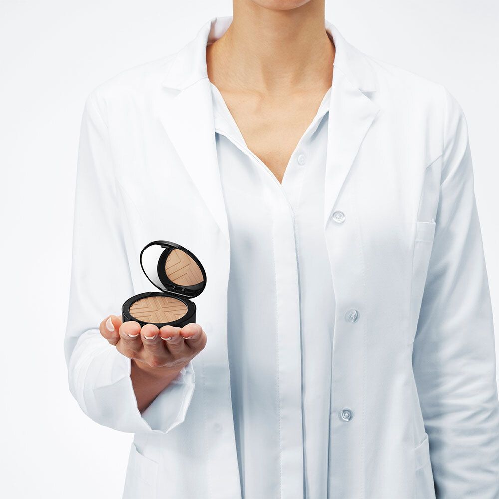 Persoon houdt open VICHY DERMABLEND Covermatte poedercompact vast. Persoon draagt witte laboratoriumjas.