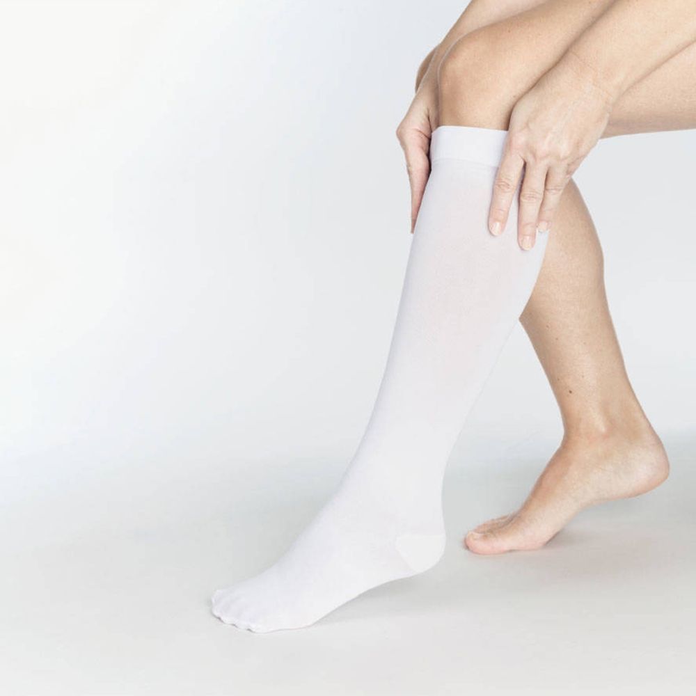 Bas blanc sur une jambe. La personne met le bas. Zone des orteils, talon et jambe visibles.