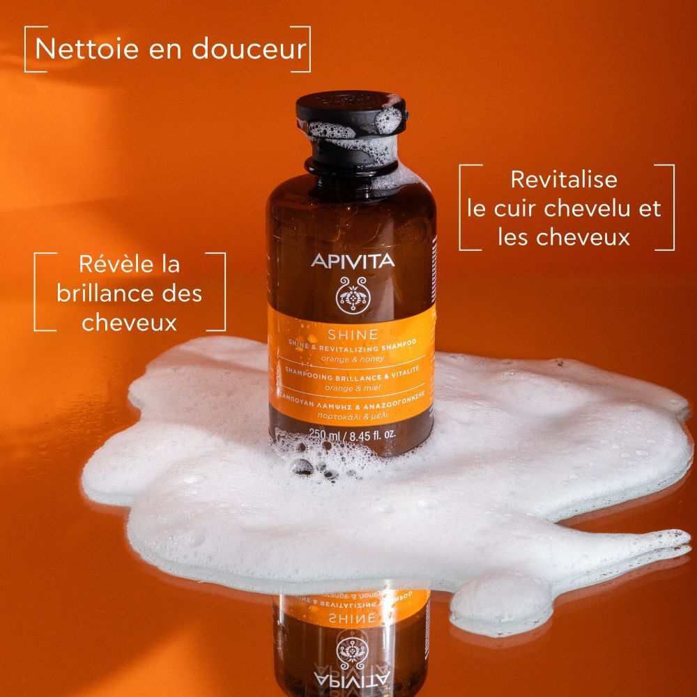 Flacon de shampooing avec mousse. Texte: APIVITA SHINE. Orange & miel. Nettoie en douceur, revitalise.