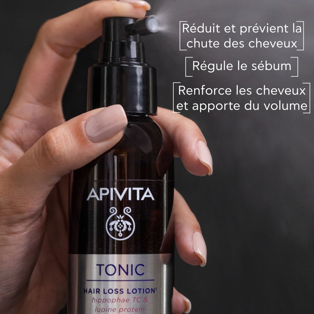Main tenant un flacon pulvérisateur. Inscriptions: APIVITA, TONIC, Hair Loss Lotion.