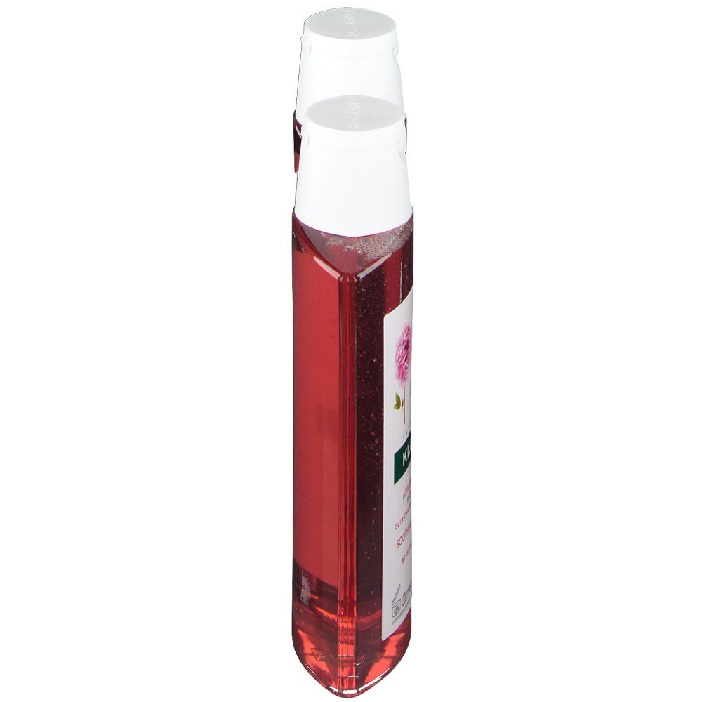 Deux flacons de shampooing, vue latérale. Bouchons blancs, flacons transparents avec liquide rouge. Nom du produit: KLORANE Shampooing à la pivoine.