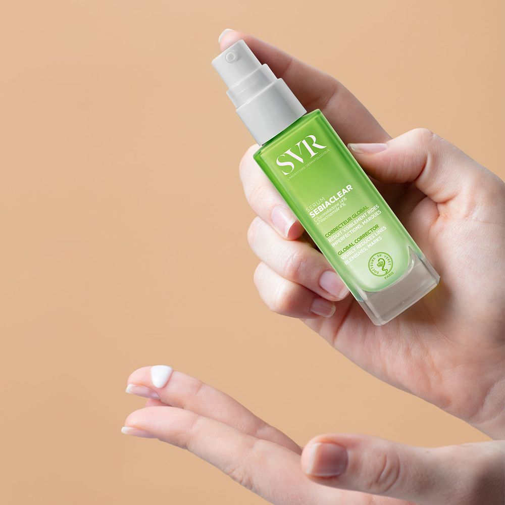 Main tenant le flacon de sérum. Inscription : SVR SEBIACLEAR Serum. Produit sur le doigt.
