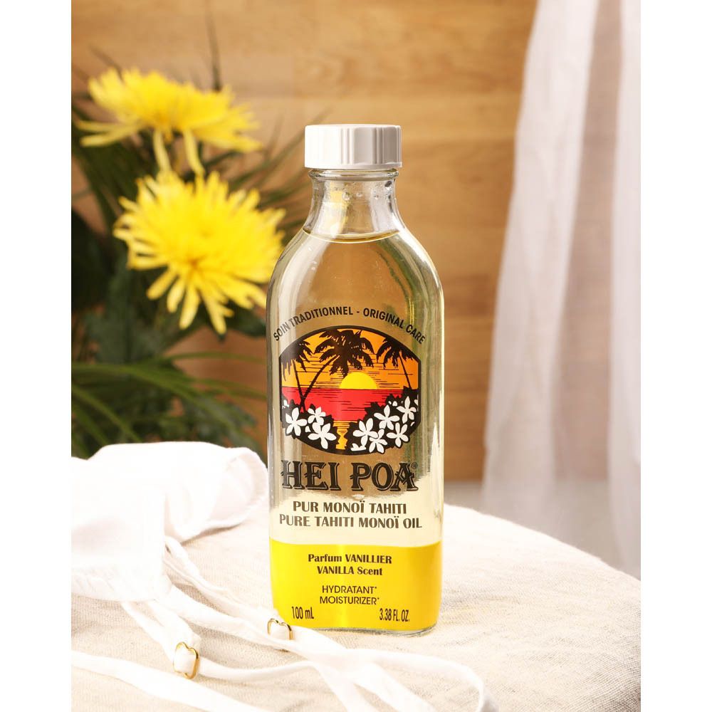 Flacon d'huile HEI POA® Vanille sur table avec fleurs jaunes et tissu blanc. Étiquette jaune, bouchon blanc. Logo coucher de soleil.
