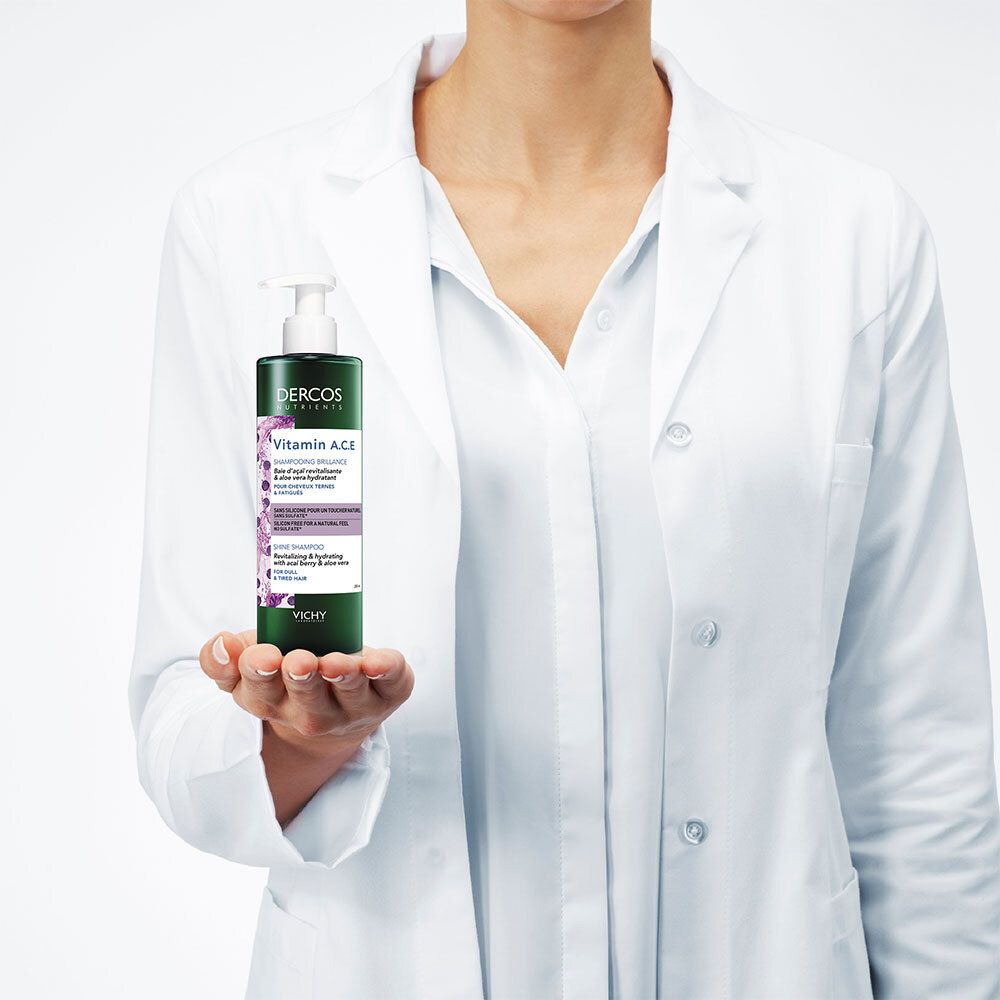 Persoon in witte jas houdt een groene shampoo fles vast. Opschrift: Dercos Nutrients Vitamin A.C.E. Shampoo.