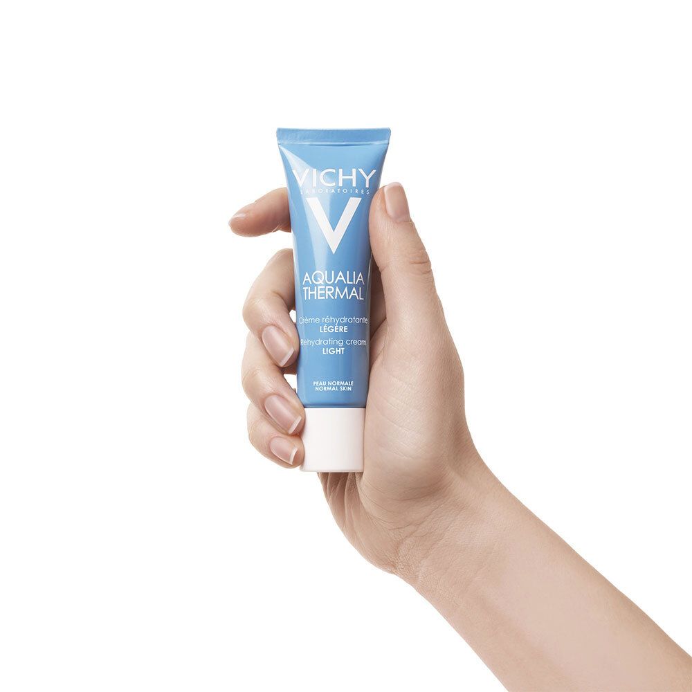 Main tenant un tube bleu Vichy Aqualia Thermal. Bouchon blanc, texte.