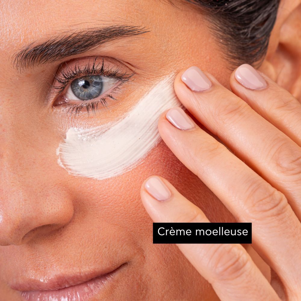 Gros plan d'une femme appliquant de la crème sur son visage. Texte : Crème moelleuse.