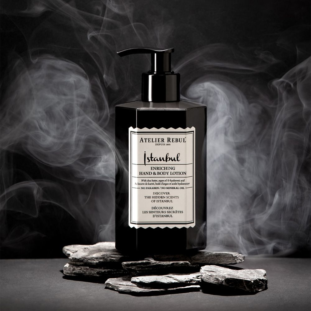 Zwarte hand- & bodylotion fles met pomp. Tekst: ATELIER REBUL Istanbul. Rokerige achtergrond.