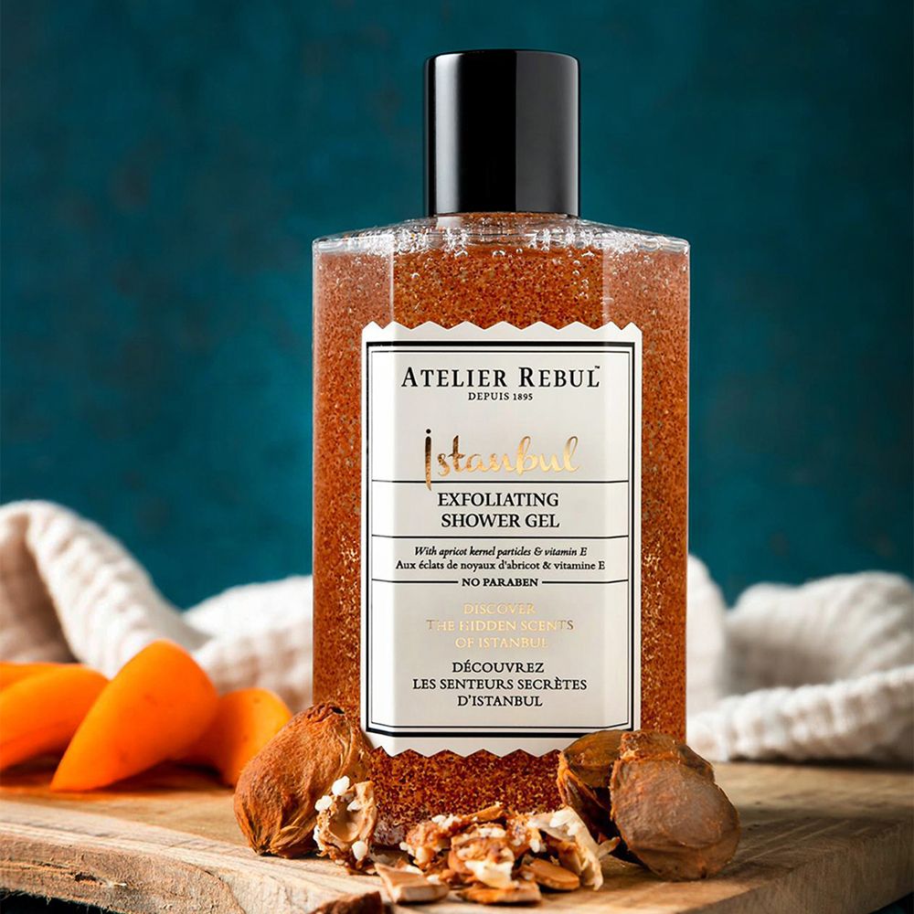 Exfoliërende douchegel. Fles met zwarte dop, op houten plank. Label met productnaam en merk.