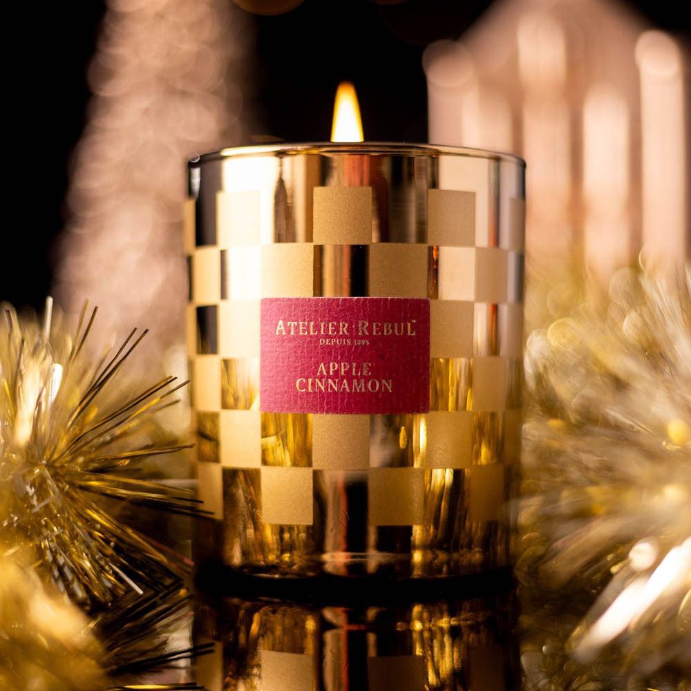 Brandende gouden kaars met dambordpatroon. Label "ATELIER REBUL", "APPLE CINNAMON".