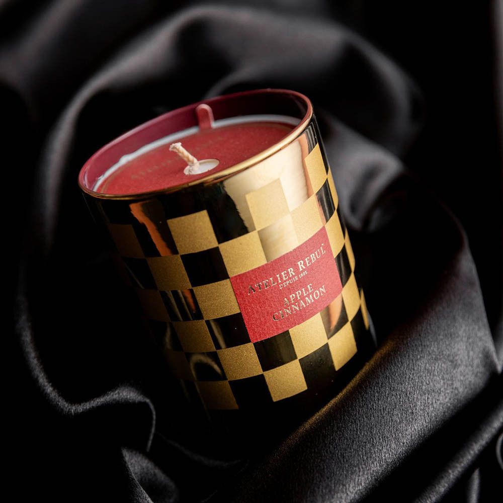 Gouden kaars met dambordpatroon. Label "ATELIER REBUL", "APPLE CINNAMON". Op zwarte stof.