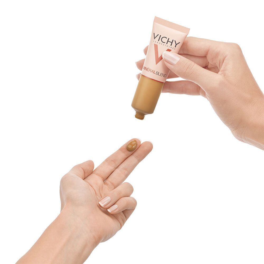 Fond de teint appliqué sur un doigt. Marque: Vichy. Liquide brun. Tube beige avec bouchon cuivré.