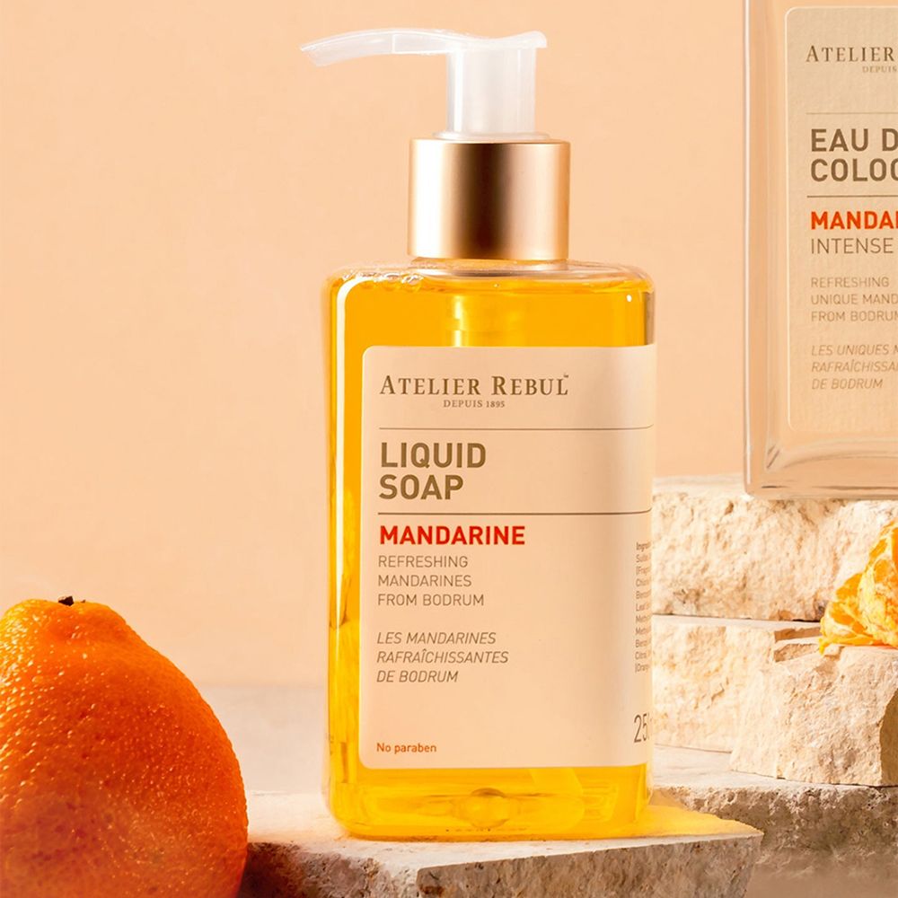 Vloeibare zeep met pomp en mandarijn. Transparante houder met oranje vloeistof. Opschrift: ATELIER REBUL, LIQUID SOAP, MANDARINE.