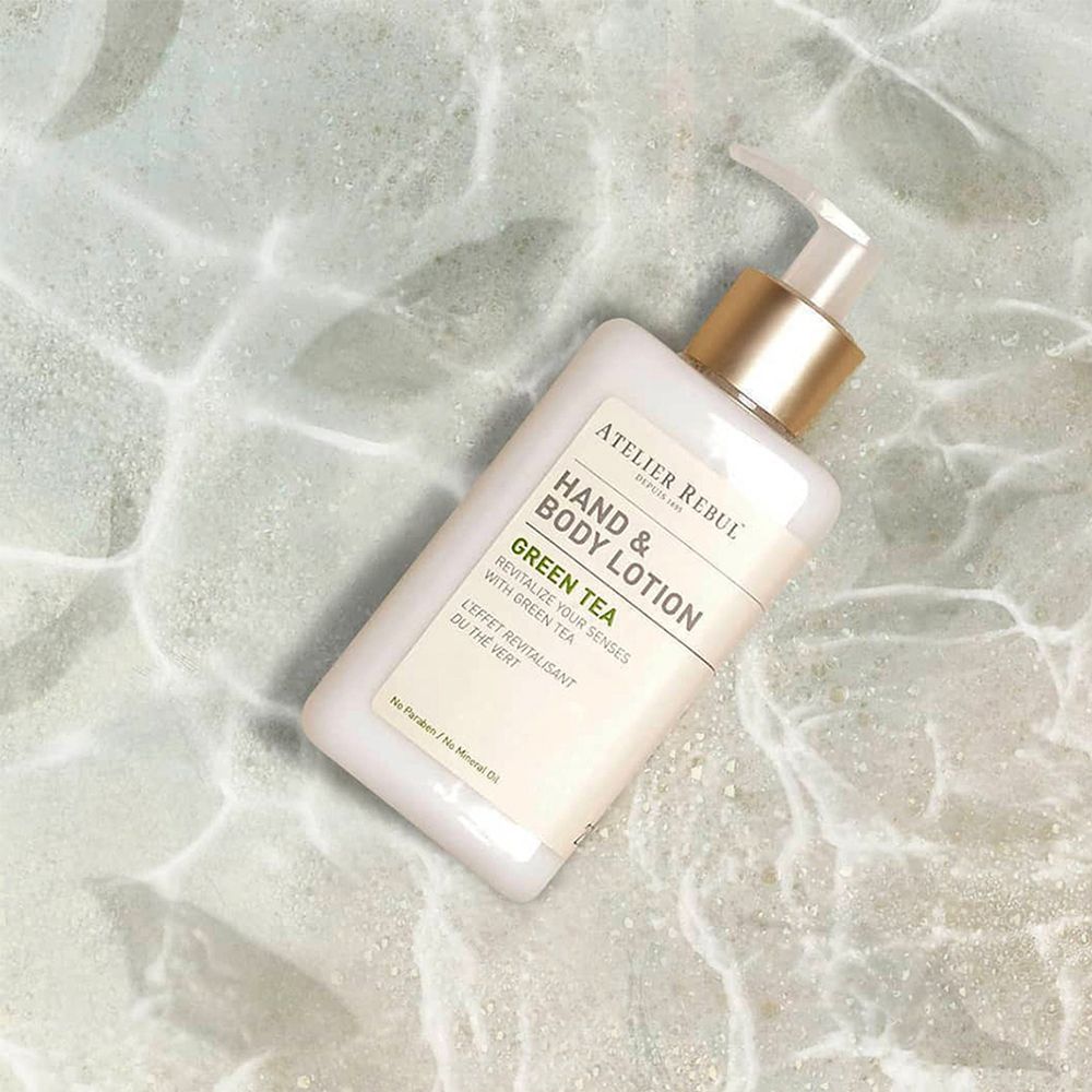 Hand- und Bodylotion-Flasche auf einer Oberfläche mit Wasseroptik. Aufschrift: ATELIER REBUL, Hand & Body Lotion, Green Tea.