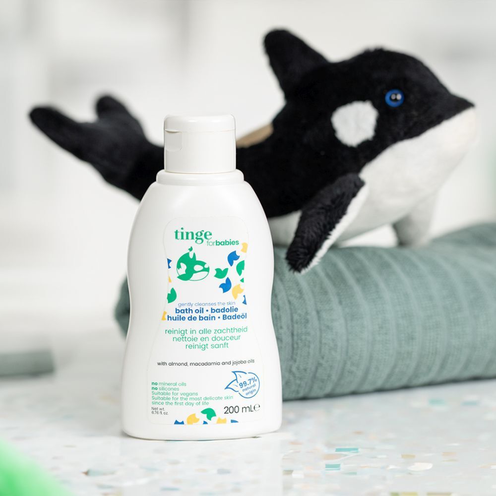 Witte fles "tinge for babies badolie" naast een knuffel. Bevat 200 ml.