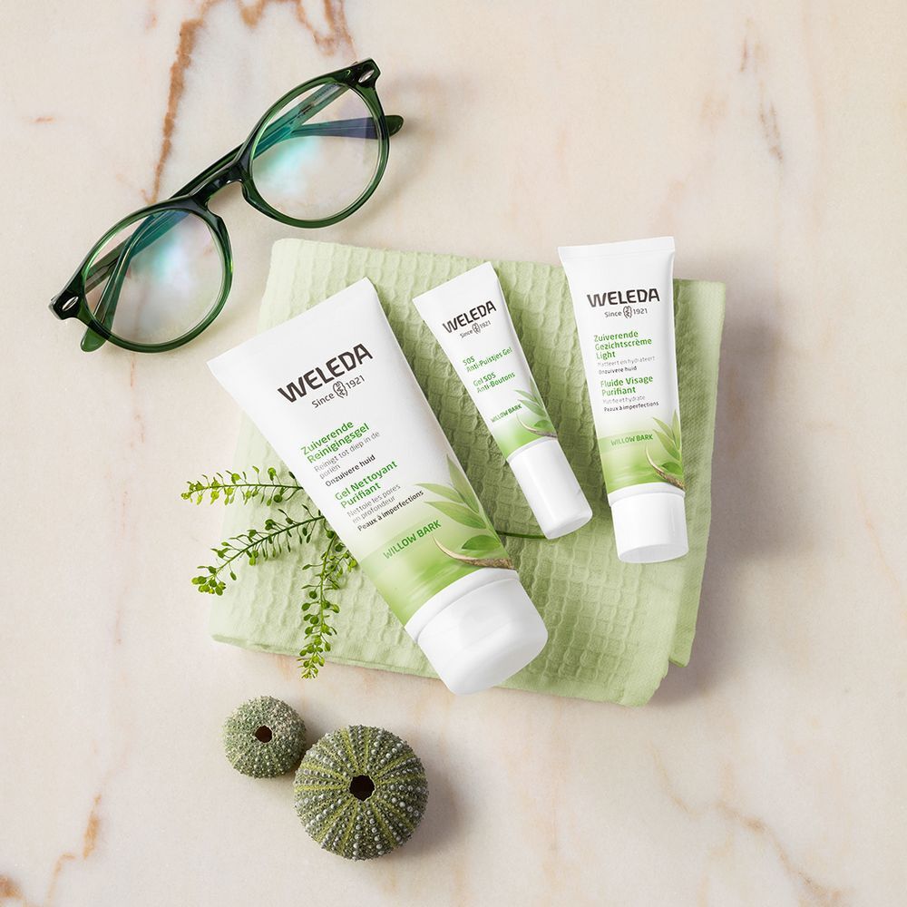 Drei Weleda-Produkte auf grünem Tuch. Brille, grüne Dekoration. Produkte: ZUIVERENDE GEZICHTSCRÈME LIGHT.