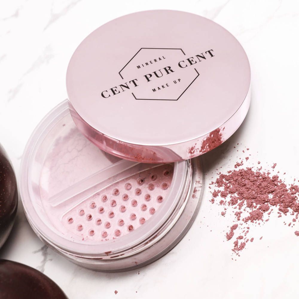 Poudre minérale rose dans un pot transparent avec couvercle rose. Couvercle avec logo. Poudre éparpillée à côté.