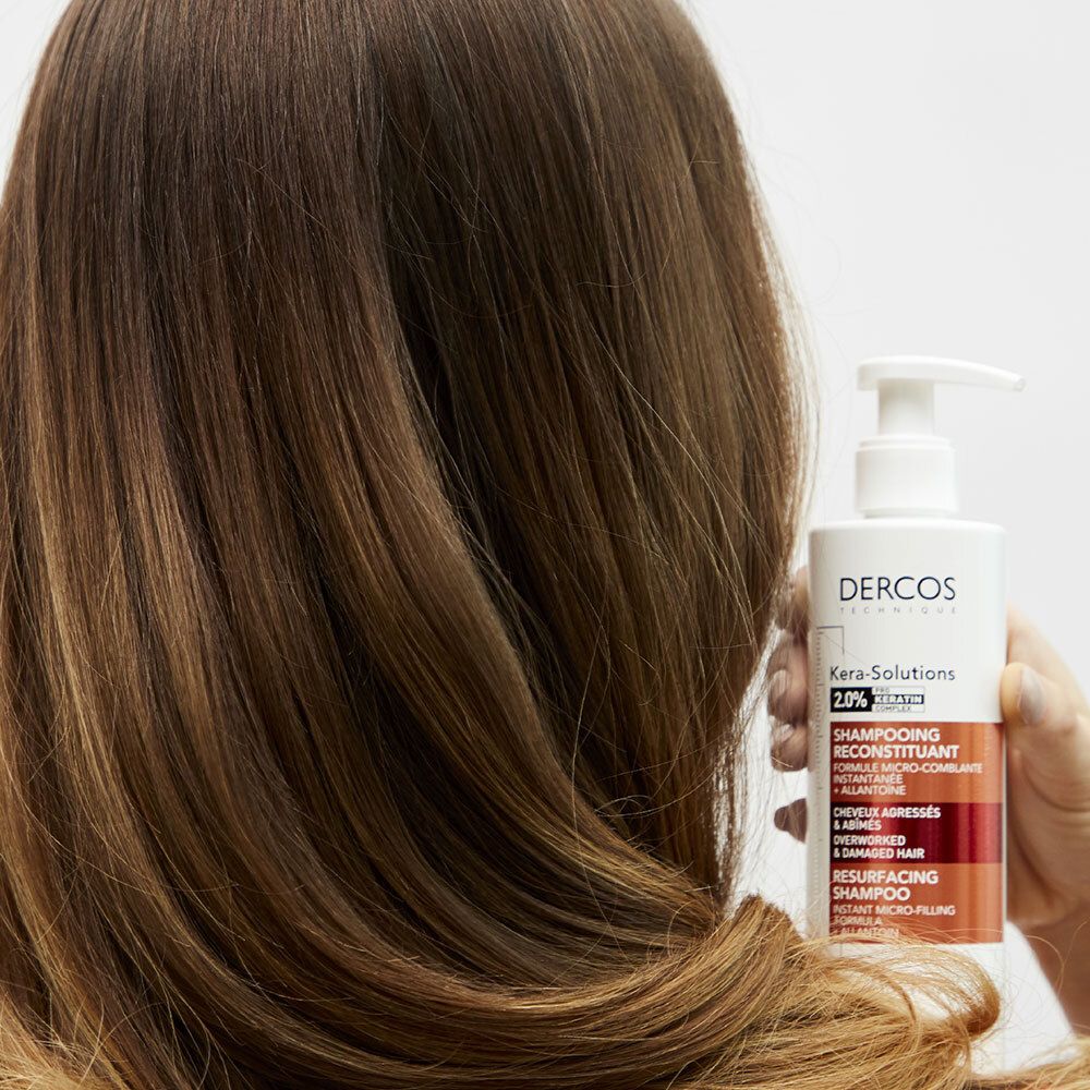 Een persoon houdt een fles shampoo vast. Het product is voor beschadigd haar.