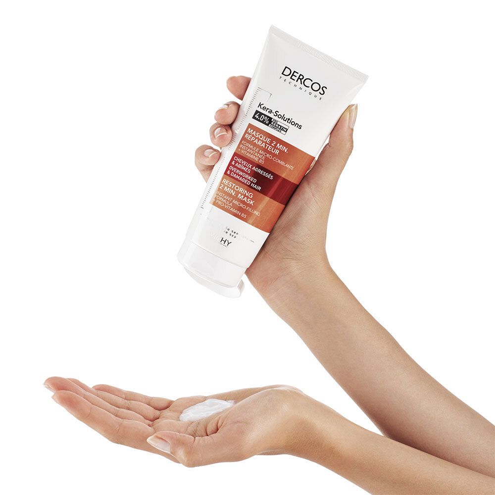 Mains tenant un tube et du produit. Inscriptions: Dercos, Kera-Solutions, Masque 2 min. réparateur. Produit dans la paume.