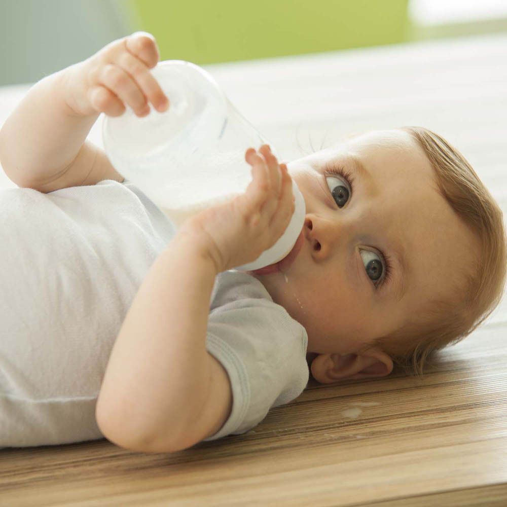 Bébé buvant d'un biberon transparent. Le bébé est allongé sur le sol.