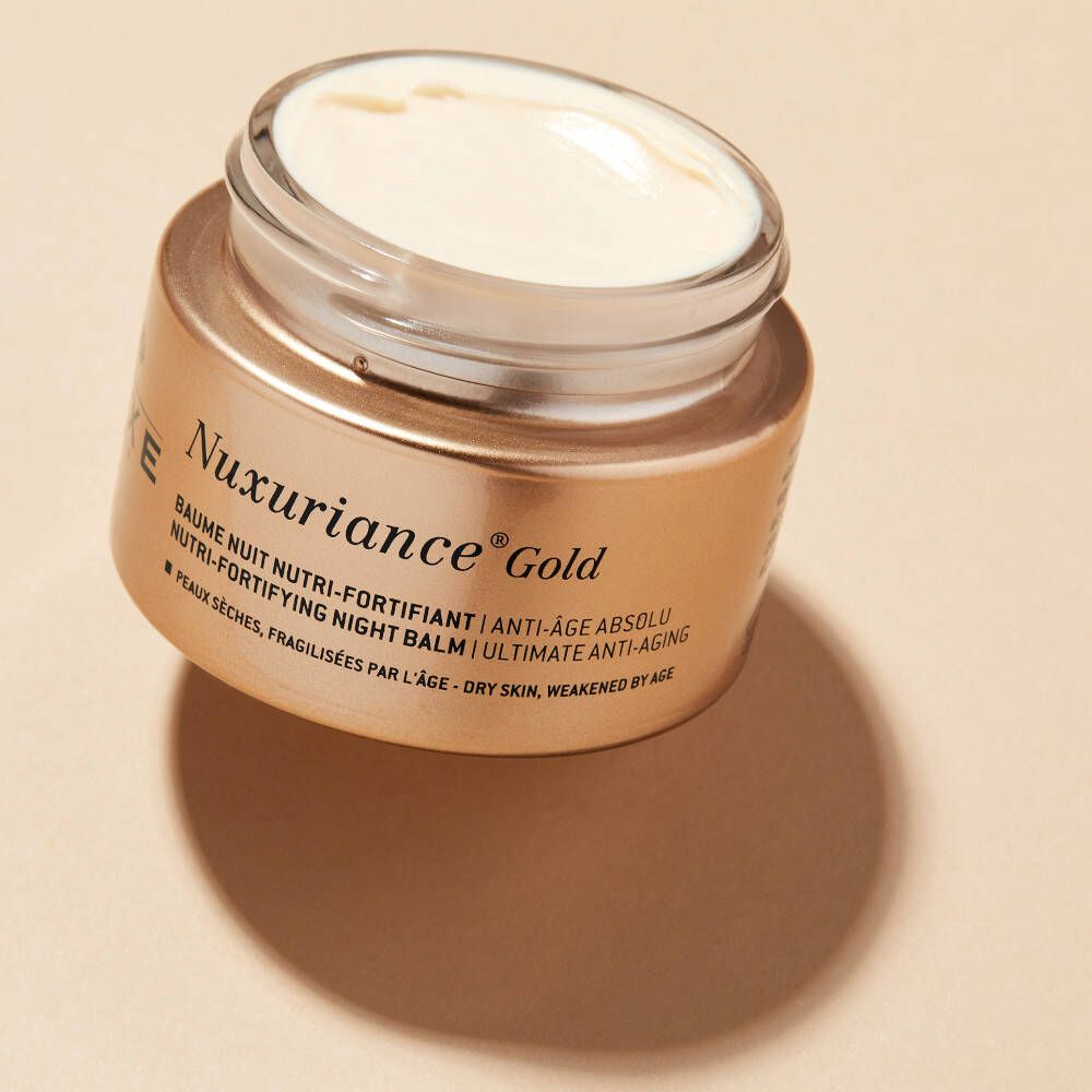 Open gouden pot met crème. Opschrift: Nuxuriance Gold, Baume Nuit Nutri-Fortifiant, Ultimate Anti-Aging.