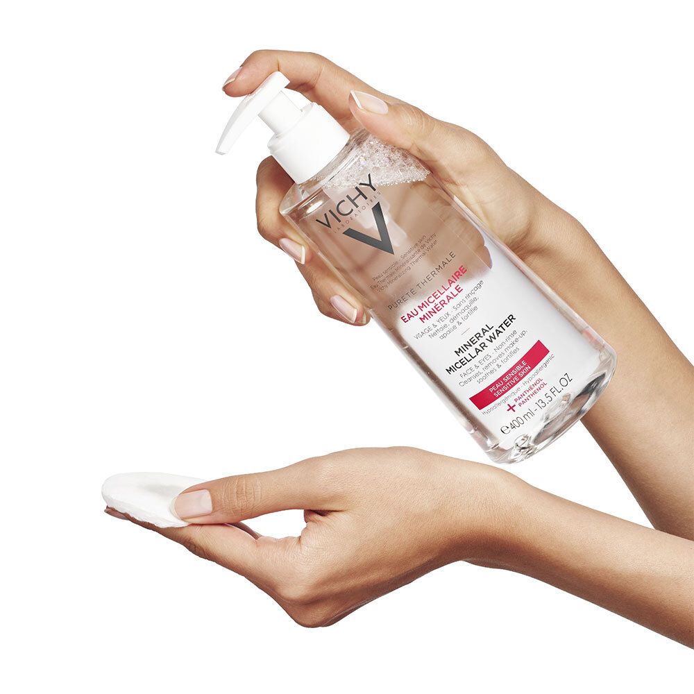 Hände halten eine Flasche Vichy Mizellenwasser und ein Wattepad. Produkt wird auf Wattepad gesprüht.