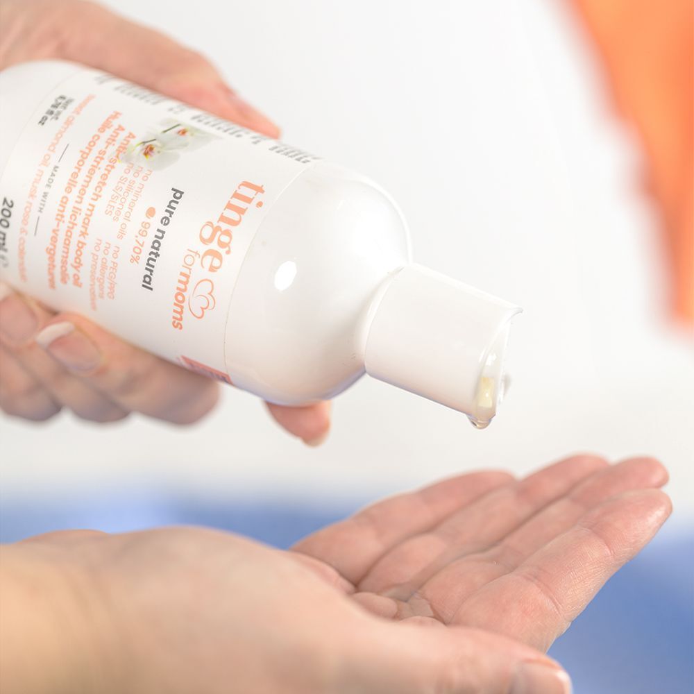 Witte fles, olie druppelt op een hand. Opschrift: tinge for moms, anti-striae olie.