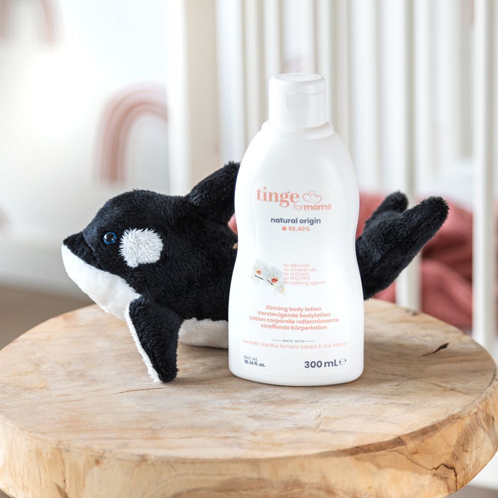 Witte fles "tinge for moms" naast een knuffelwalvis op een houten sokkel. 300 ml.