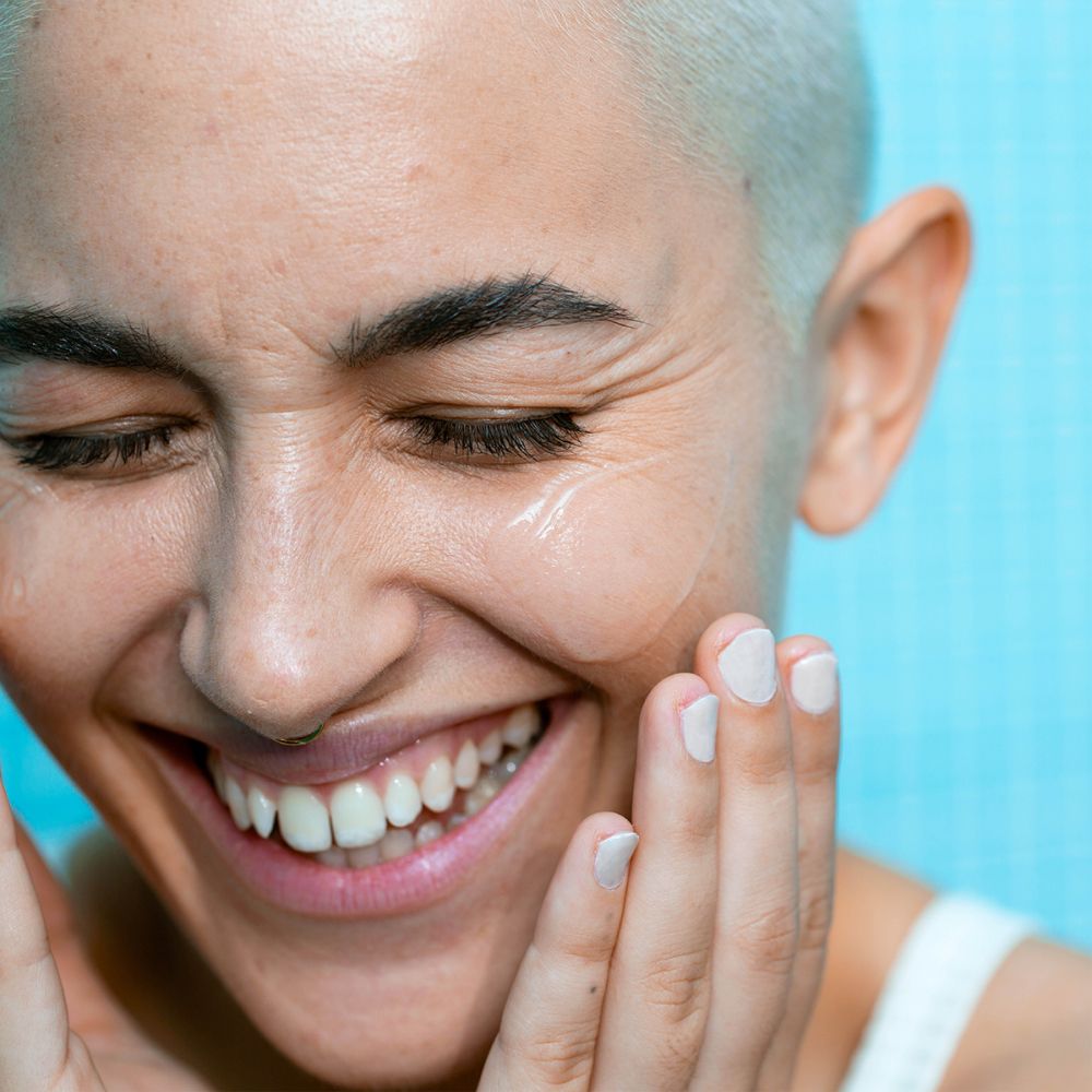 Gros plan d'une personne appliquant du gel sur son visage. La personne sourit.