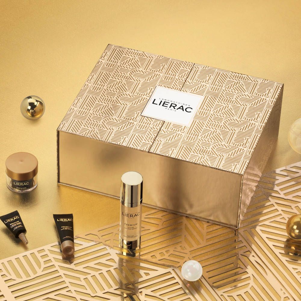 Goldene Geschenkbox mit Kosmetikprodukten und Dekoration. Produkte: Serum, Creme, Tuben. Marke: LIERAC. Hintergrund: Gold.