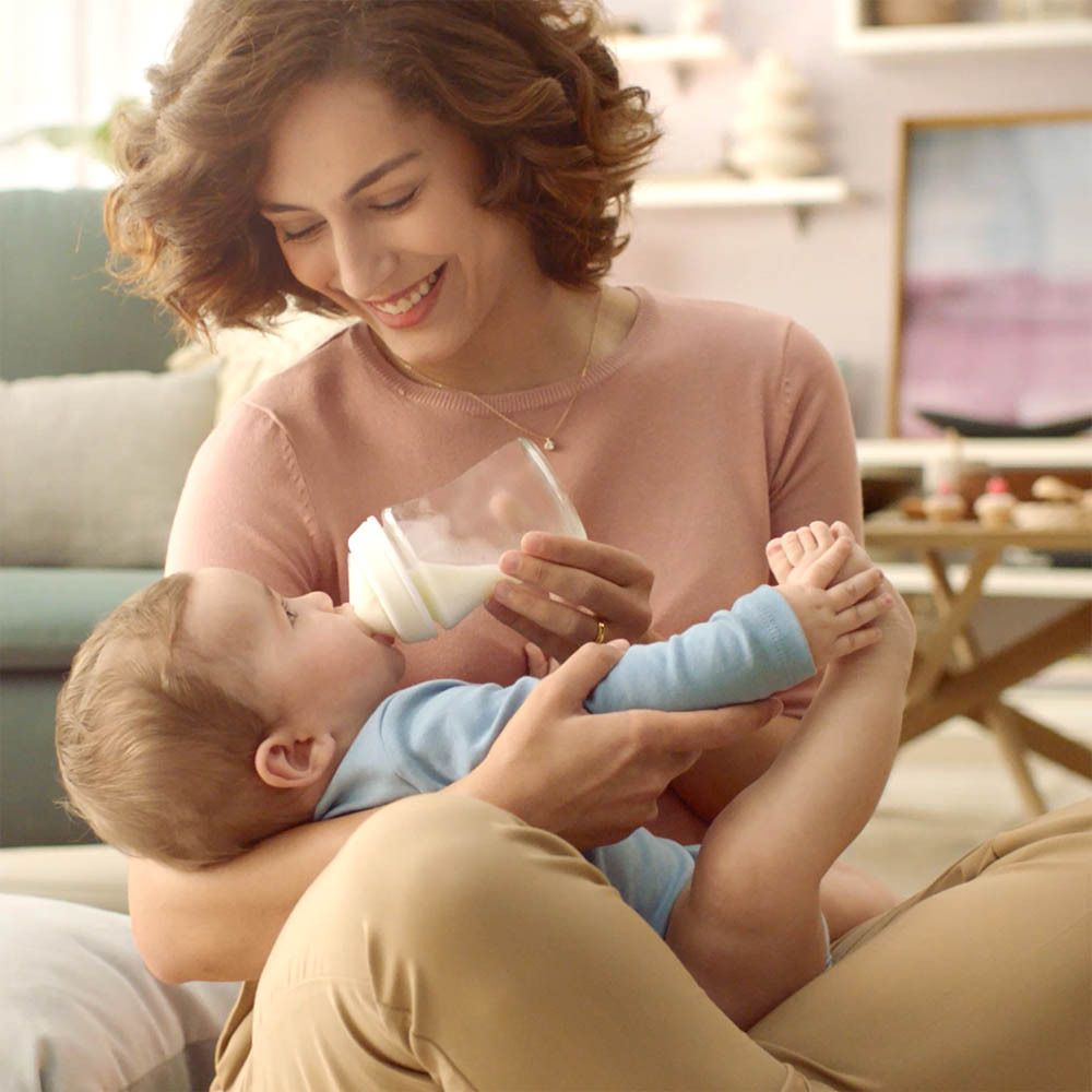 Une femme nourrit un bébé avec un biberon. Le biberon est en verre et contient un liquide blanc.