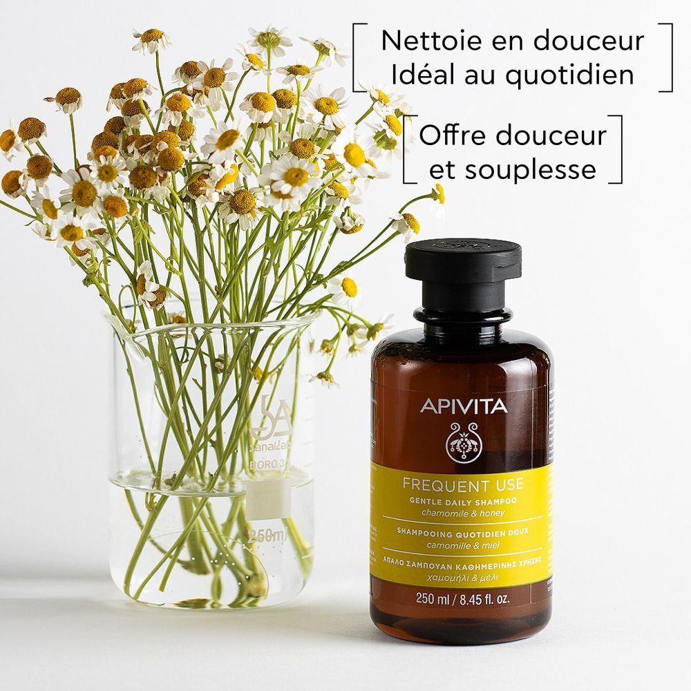Flacon à côté d'un vase avec des fleurs. Texte : Nettoie en douceur. Marque : Apivita. Shampooing.