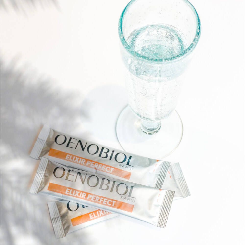 Drei Beutel Oenobiol Elixir Perfect neben einem Glas Wasser. Produktname und Logo deutlich sichtbar.