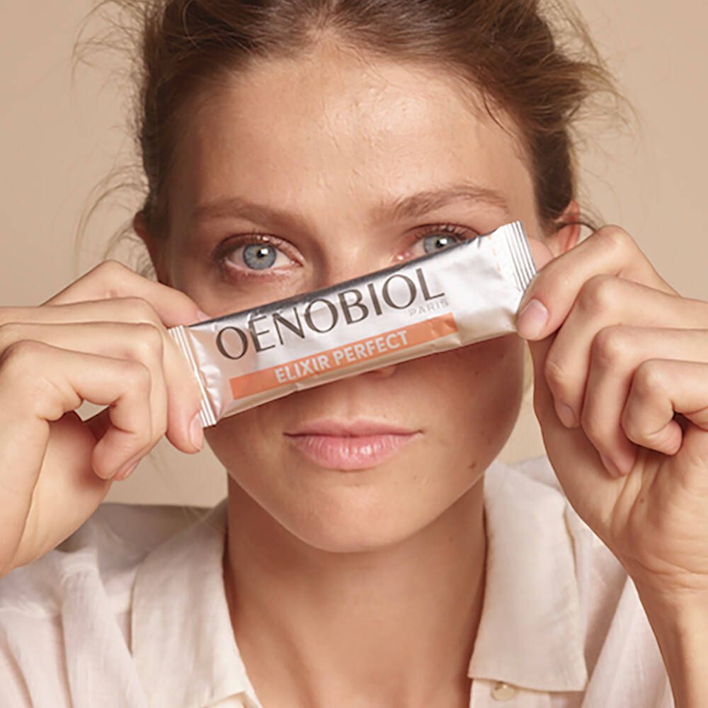 Frau hält einen Beutel Oenobiol Elixir Perfect vor ihr Gesicht. Produktname und Logo sind sichtbar.