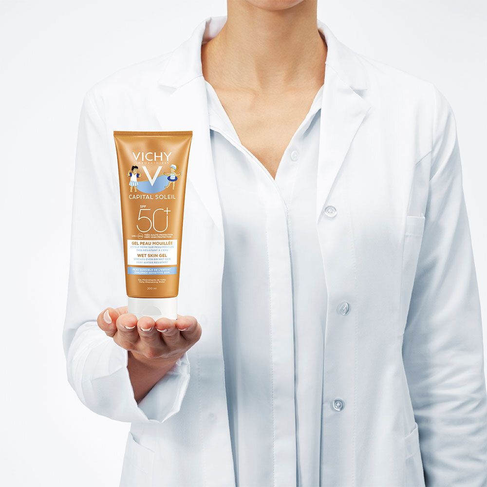 Personne tenant un tube de crème solaire. Marque Vichy, SPF 50+. La personne porte une blouse blanche.