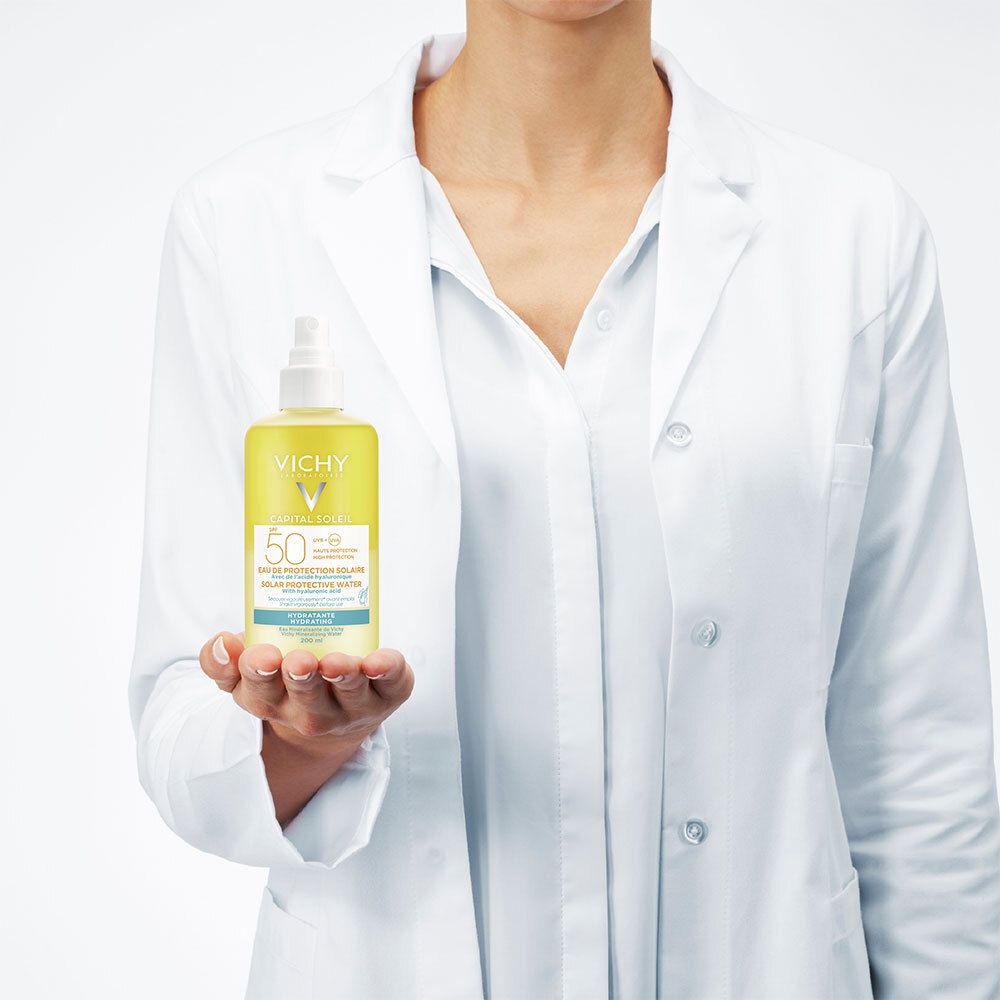 Persoon in witte jas houdt gele fles. Vichy Capital Soleil SPF50.