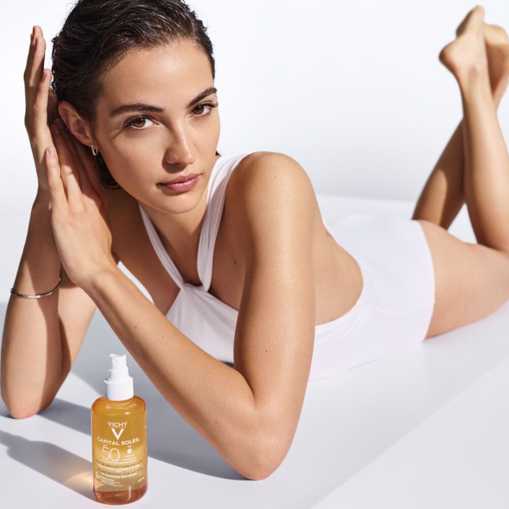 Femme allongée, à côté d'elle un flacon Vichy Capital Soleil Eau de protection solaire SPF50.