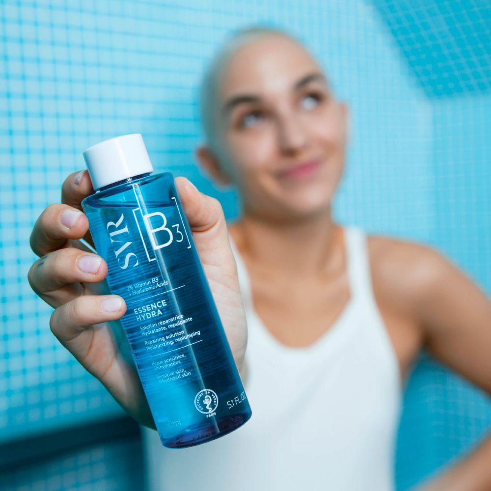 Flacon bleu avec bouchon blanc. Inscription : SVR [B3] ESSENCE HYDRA. Contient 2% Vitamine B3 + Acide Hyaluronique. Pour peaux sensibles, déshydratées.