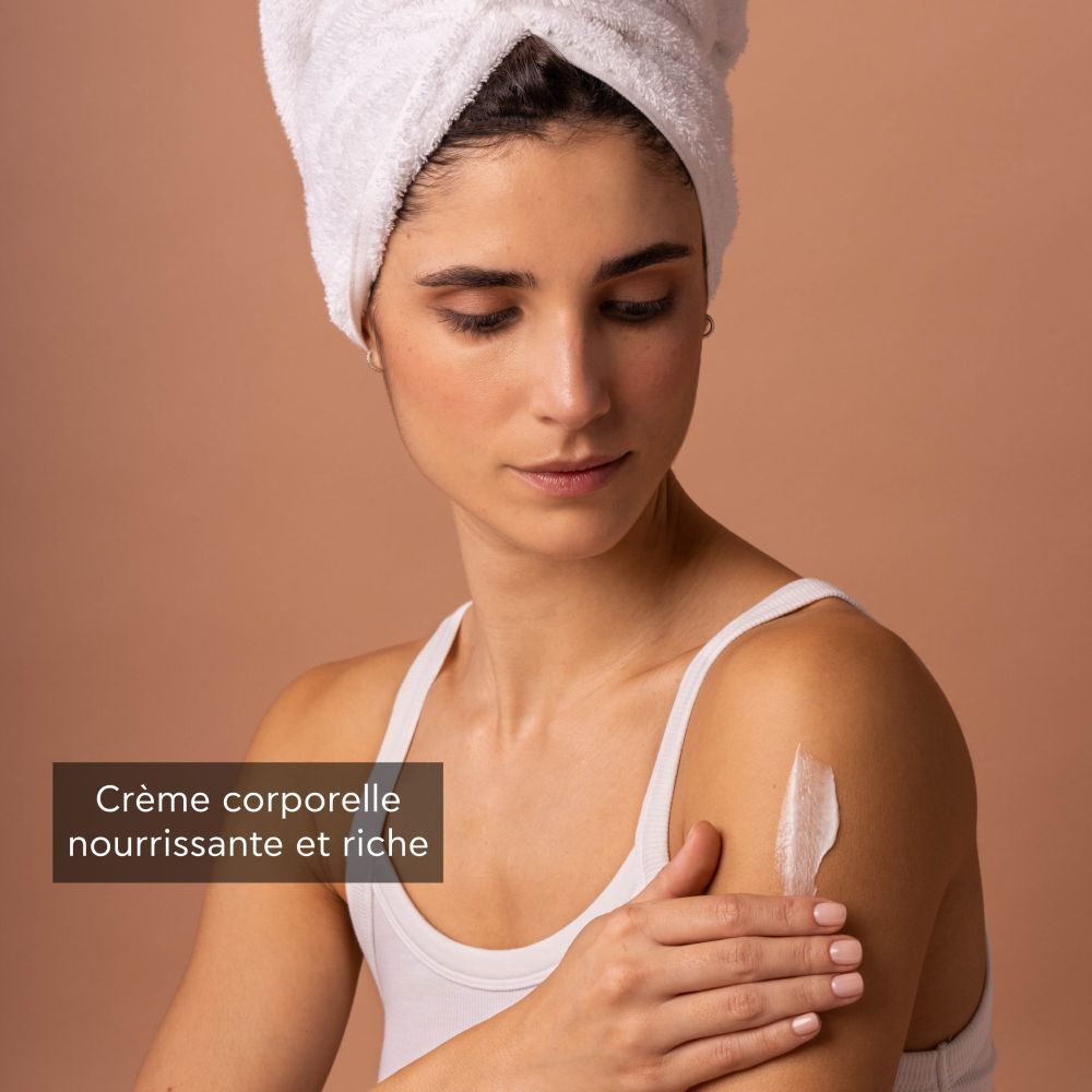 Femme appliquant de la lotion pour le corps. Inscription : APIVITA, ROYAL HONEY. Débardeur blanc, serviette sur la tête.