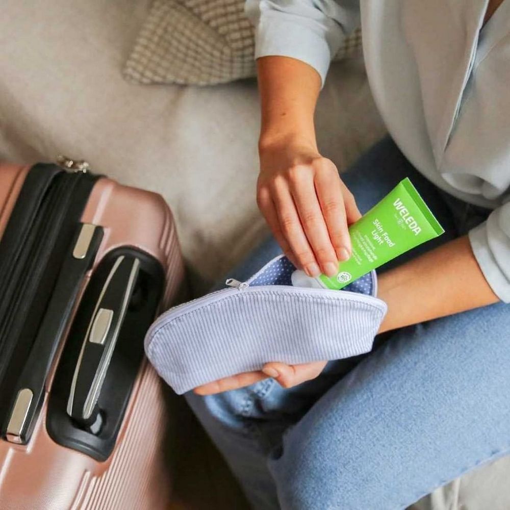 Personne tenant un tube vert Skin Food Light d'une trousse de toilette. Valise en arrière-plan.