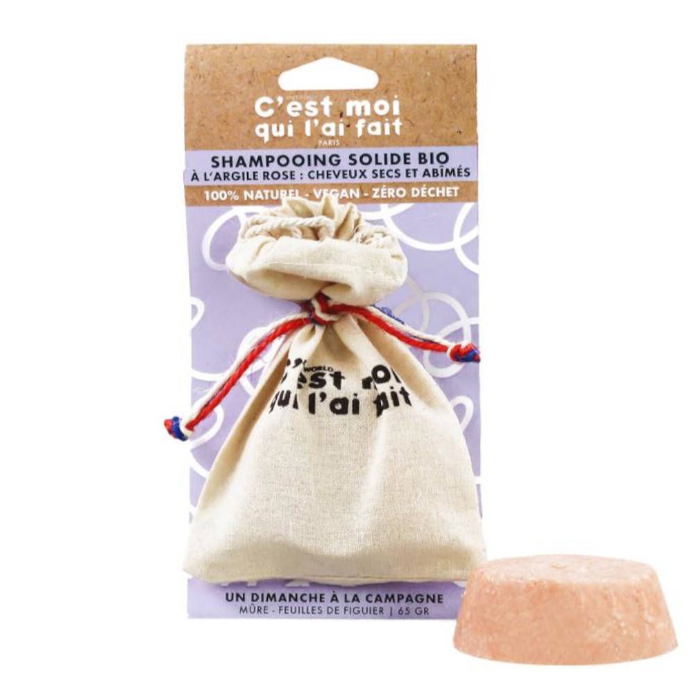 Shampooing solide rose, rond, à côté d'un sac en lin avec cordon. Sur l'emballage: marque, nom du produit, texte.