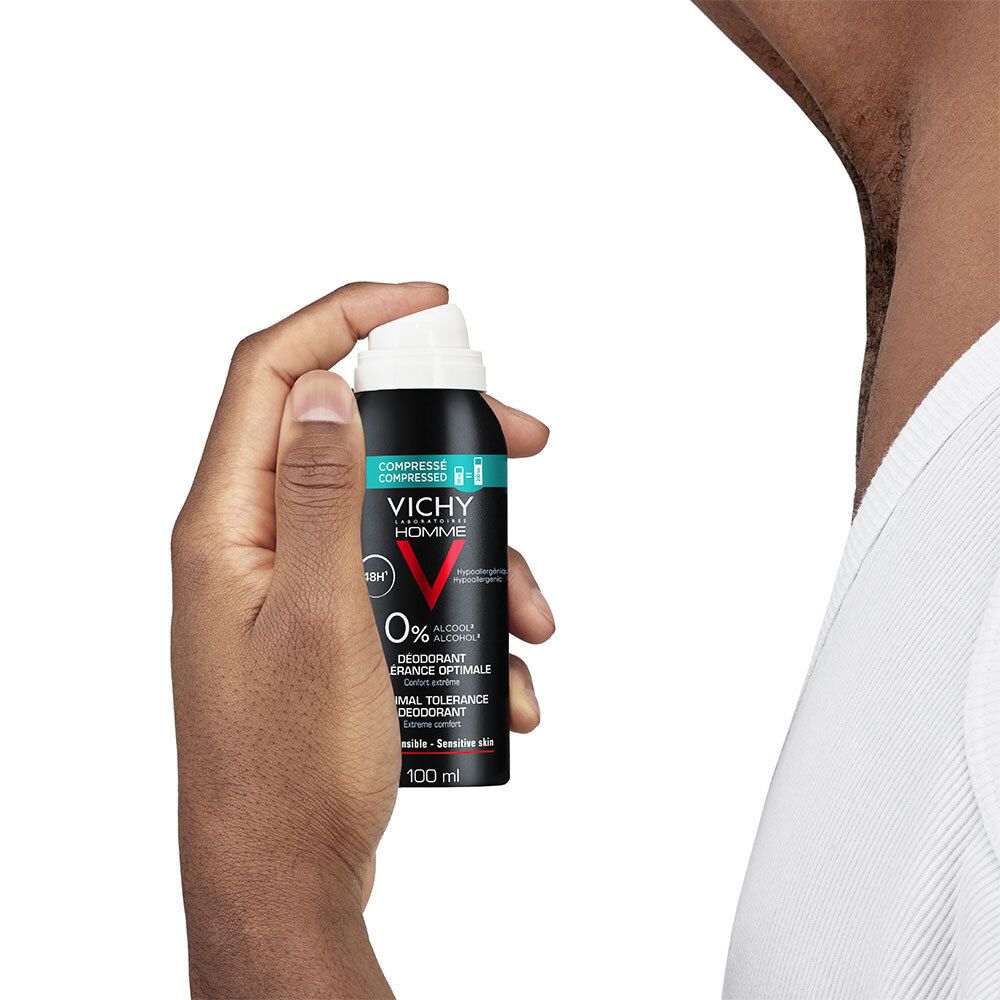 Persoon houdt deodorant sprayfles vast. Zwarte fles, witte sproeikop. Tekst: Vichy Homme, 48H, 0% alcohol.