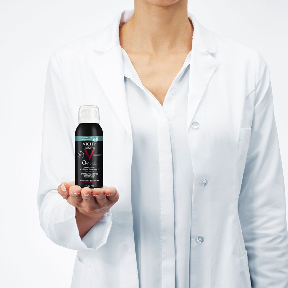 Persoon in witte jas houdt deodorant sprayfles vast. Zwarte fles, witte sproeikop. Tekst: Vichy Homme.