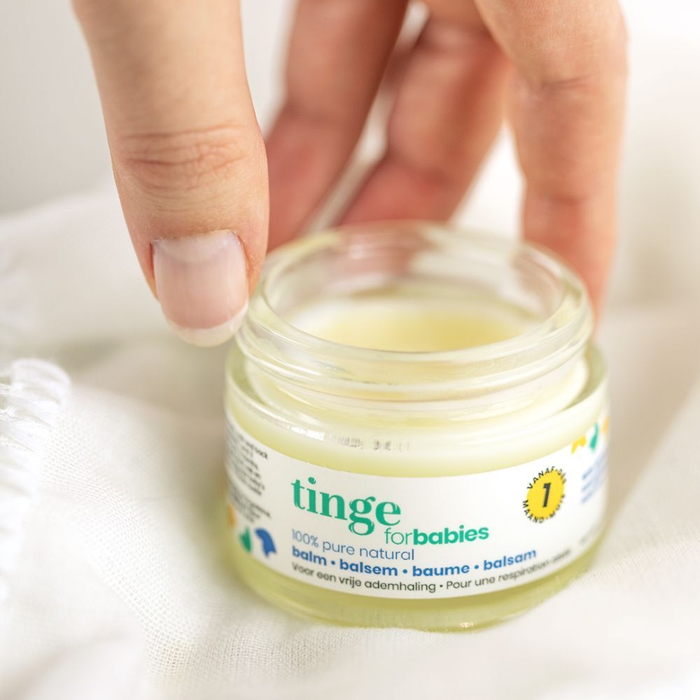 Pot de baume Tinge for babies, couvercle blanc. Inscription : 100% naturel. Main tenant le pot.