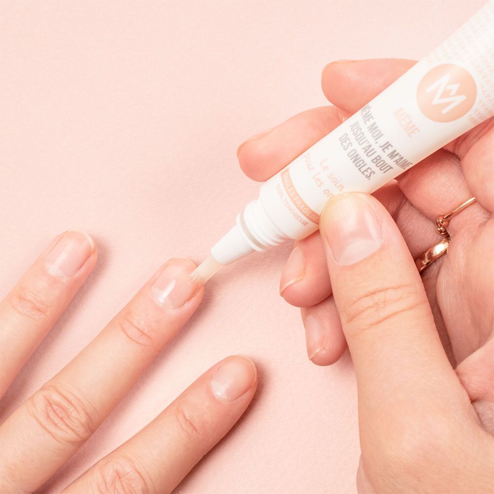 Toepassing van de nagelverzorgingscrème. Hand met vinger waarop de crème wordt aangebracht. Roze achtergrond.