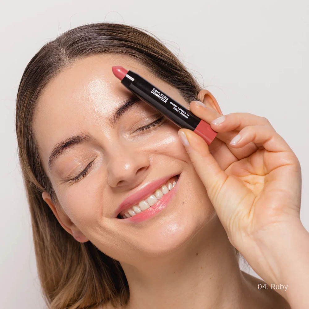 Les Couleurs de Noir Chubby LipBalm 04 Ruby. Femme tenant le bâton. Baume à lèvres sur les lèvres.