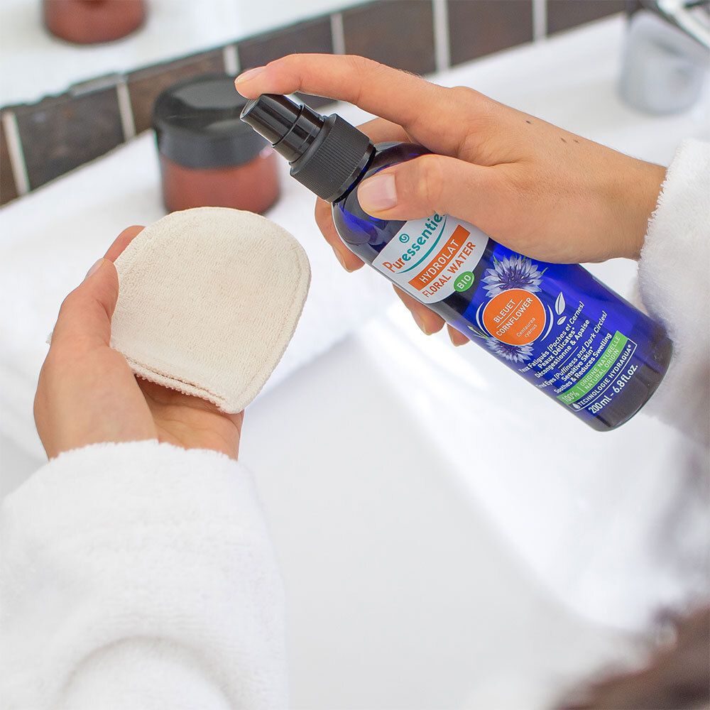 Personne tient flacon et coton. Flacon: Puressentiel, Hydrolat Floral Water, Bio. Arrière-plan: lavabo.